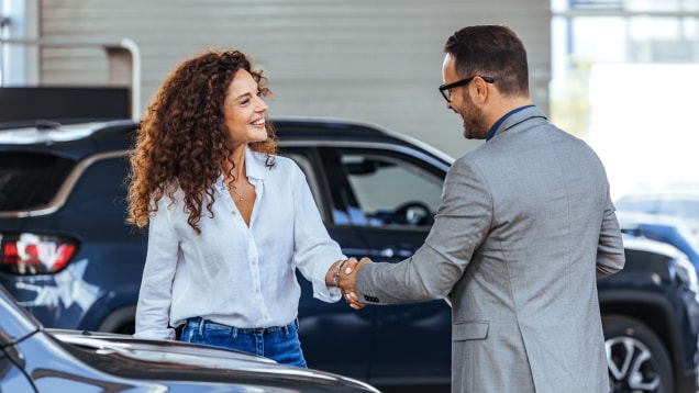 Executive and happy woman shake hands at car dealership