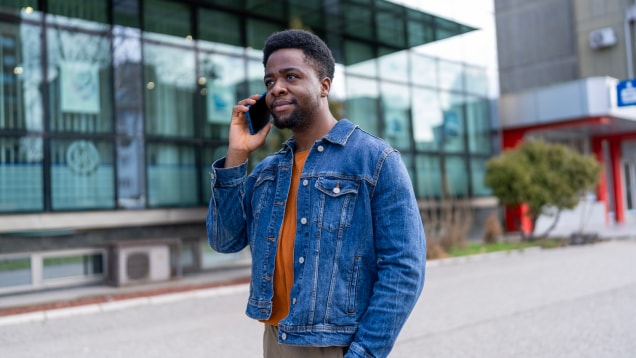 A young African American man participates in an active phone conversation while walking.