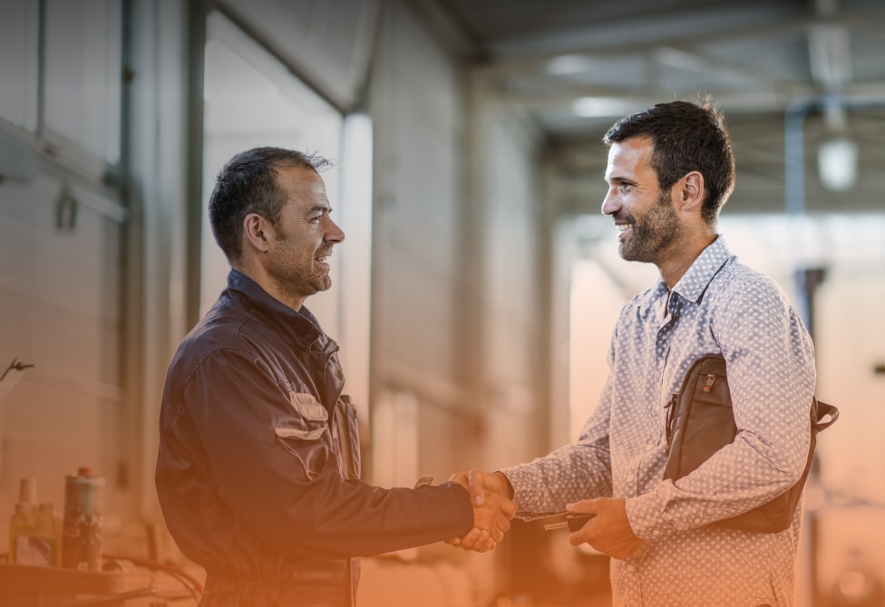 Happy car mechanic shaking hands with his customer in auto repair shop