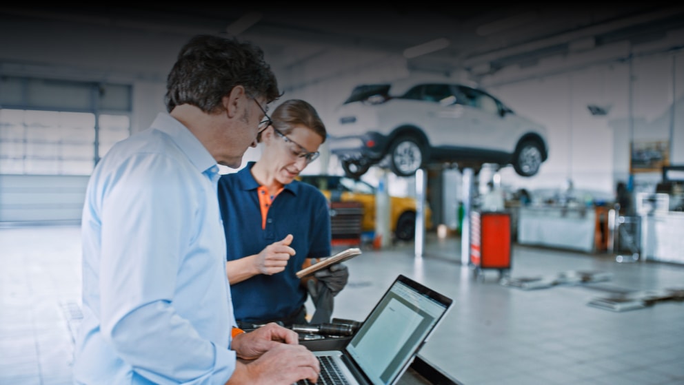 Manager And Mechanic Using A Laptop And Mobile Phone At Car Workshop