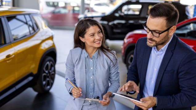 A man and woman are engaged with a tablet in a car dealership