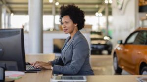 A woman at a car dealership, working on a computer at her desk