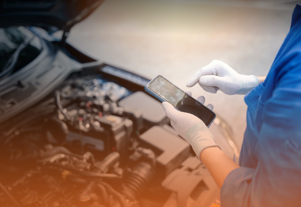 Mechanic with mobile phone examining car engine at auto repair shop.