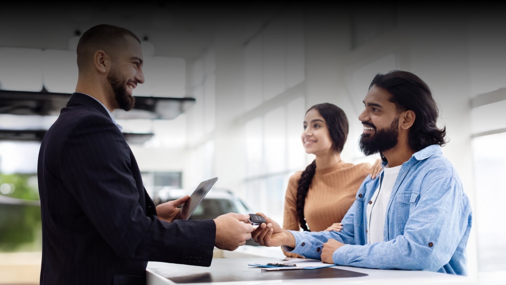 Smiling Couple Receives Car Keys From manager in Dealership shop