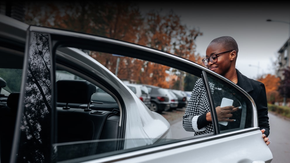 Woman getting into the back seat of a car with a mobile phone in her hand