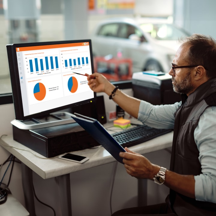 A man in a car repair shop working at a computer displaying graphs