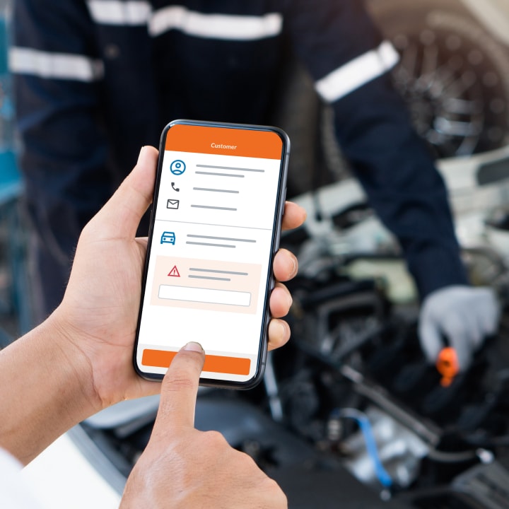 A man inspects his car's engine while checking information on his smartphone.