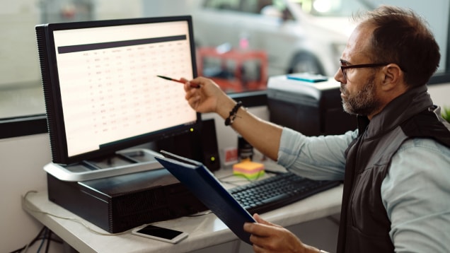 Auto mechanic analyzing reports while working on desktop PC in the office