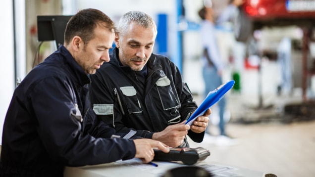Auto mechanics cooperating while going through diagnostic list in a repair shop.