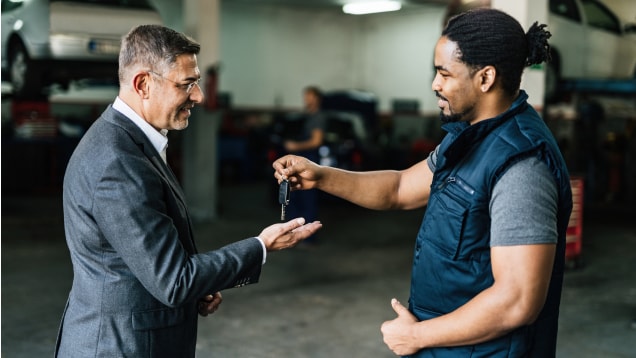 Happy auto mechanic giving car key to his customer in a repair shop
