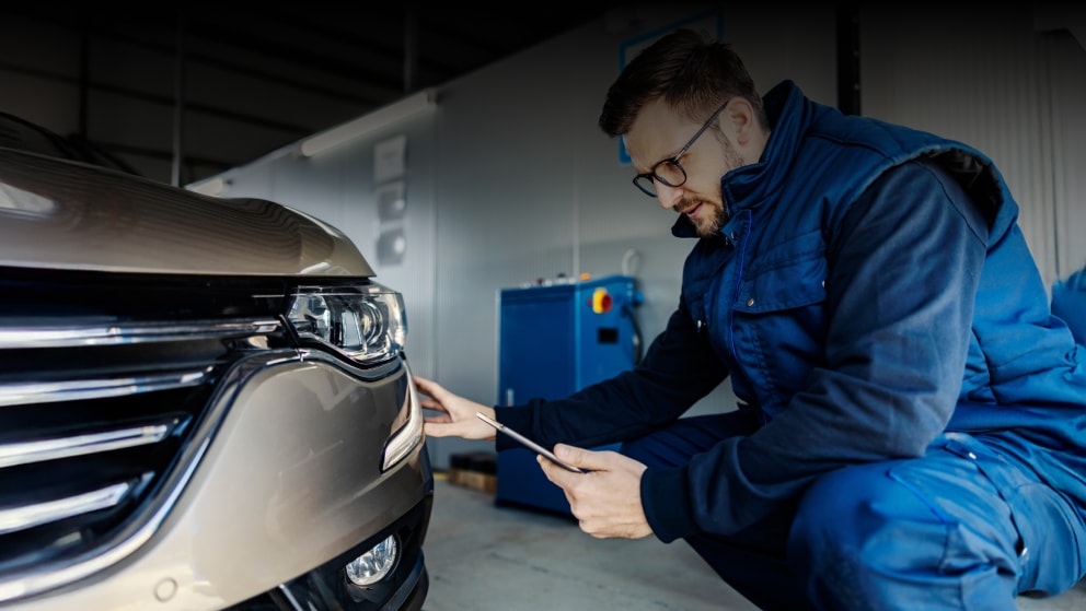 An inspector kneeling and does technical inspection of car at workshop