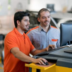 Two men collaborate on a computer inside a car repair shop